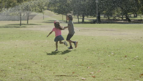 Glückliche-Kinder,-Die-Im-Sommerpark-Unter-Sprinkleranlage-Laufen